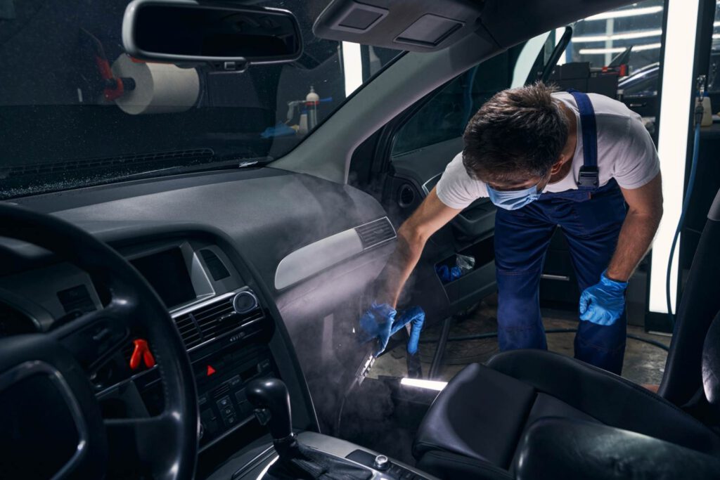 Worker of auto repair in mask bending and blowing chemical cleaning spray on car interior